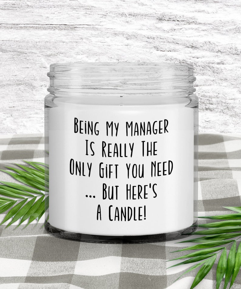 Op de afbeelding: Een witte kaars in een glazen pot met een zwart etiket waarop staat: "Manager zijn is echt het enige cadeau dat je nodig hebt... maar hier is een kaars!"