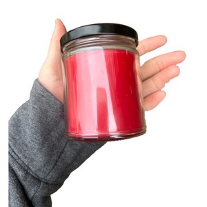 Puede incluir: Una vela roja en un tarro de vidrio transparente con tapa negra.