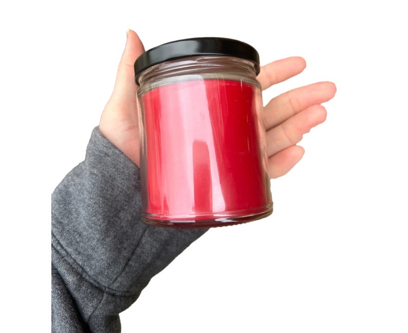 Puede incluir: Una vela roja en un tarro de vidrio transparente con tapa negra.