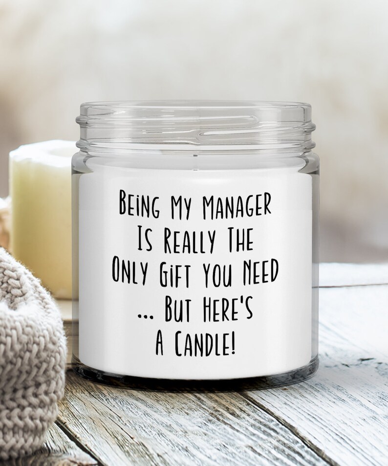 Op de afbeelding: Een witte kaars in een glazen pot met een zwart tekstlabel waarop staat: "Manager zijn is echt het enige cadeau dat je nodig hebt... maar hier is een kaars!"