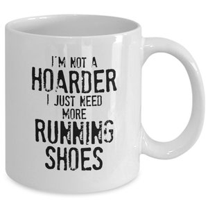 May include: White ceramic coffee mug with black text that reads "I'm not a hoarder I just need more running shoes".