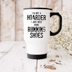 May include: White travel mug with a black handle and black lid. The mug has black text that reads "I'm not a hoarder I just need more running shoes."