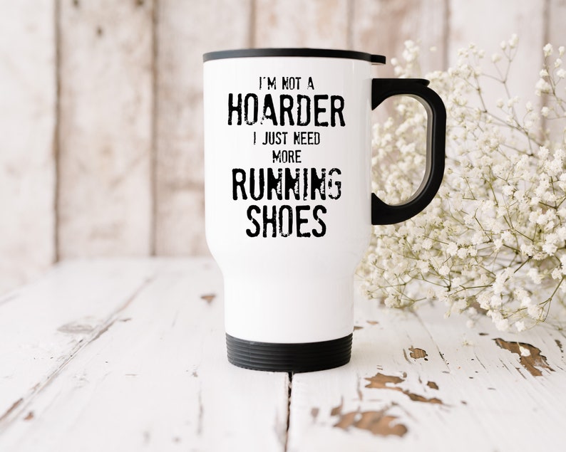 May include: White travel mug with a black handle and black lid. The mug has black text that reads "I'm not a hoarder I just need more running shoes."