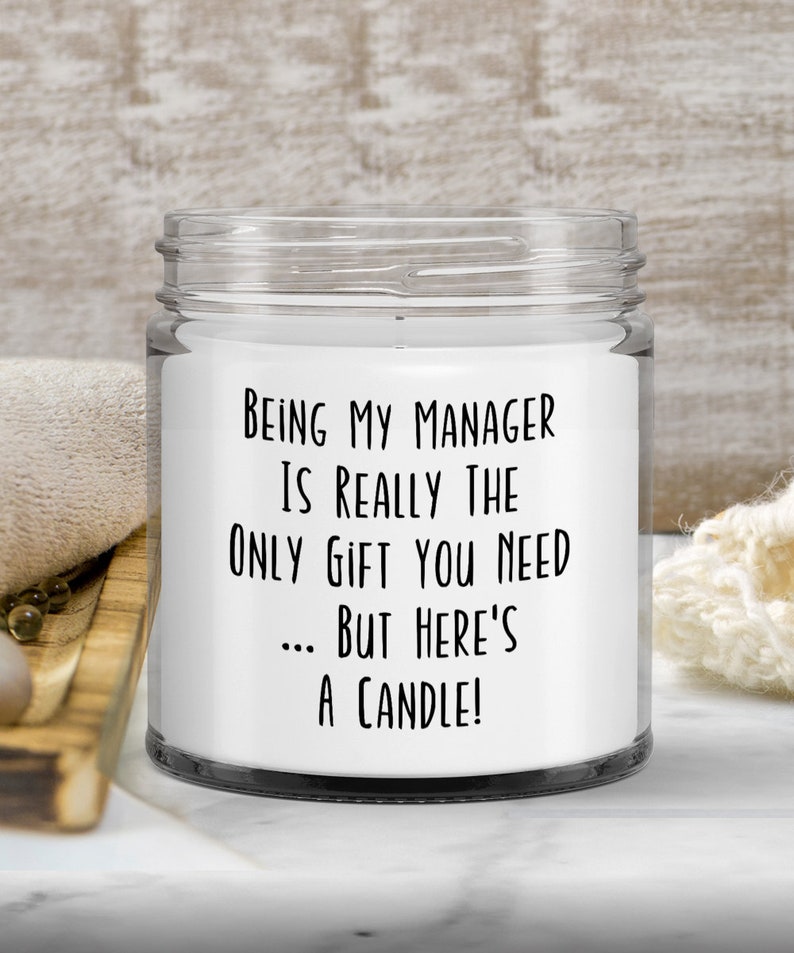 Op de afbeelding: Een witte kaars in een glazen pot met een zwart etiket waarop staat: "Manager zijn is echt het enige cadeau dat je nodig hebt... maar hier is een kaars!"