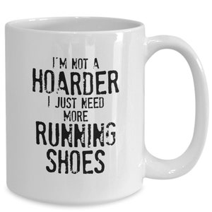 May include: White ceramic coffee mug with black text that reads "I'm not a hoarder I just need more running shoes".