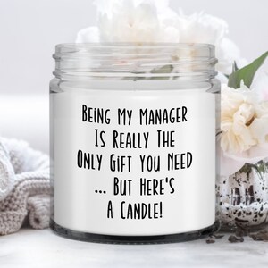 Op de afbeelding: Witte kaars in een glazen pot met een zwart etiket waarop staat: "Manager zijn is echt het enige cadeau dat je nodig hebt... maar hier is een kaars!"