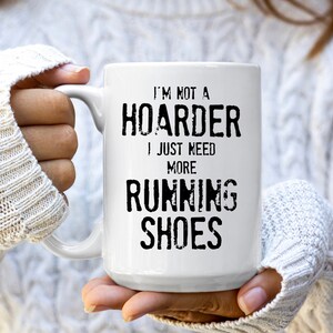 May include: White ceramic coffee mug with black text that reads "I'm not a hoarder I just need more running shoes".