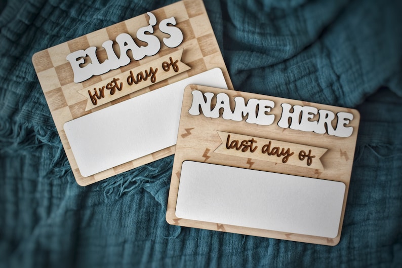 May include: Two wooden signs with blank spaces for writing. The top sign has a checkered background and says "ELIAS'S first day of". The bottom sign has a lightning bolt pattern and says "NAME HERE last day of".
