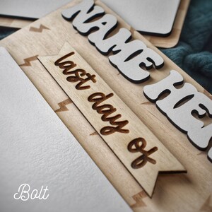 May include: A wooden sign with the words "Name Here" and "Last Day Of" in white letters. The sign has a lightning bolt pattern and is made of light brown wood.