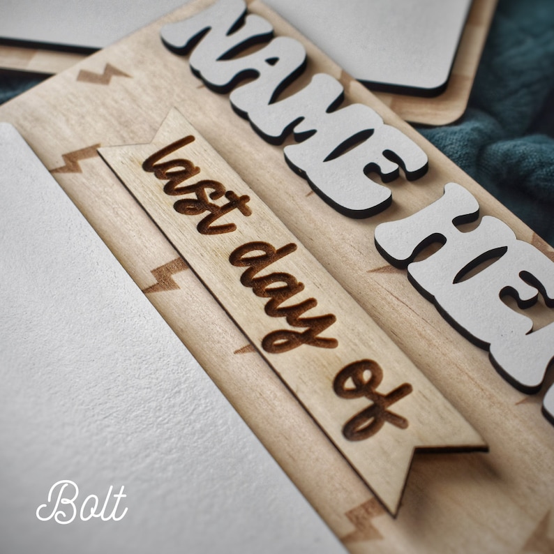May include: A wooden sign with the words "Name Here" and "Last Day Of" in white letters. The sign has a lightning bolt pattern and is made of light brown wood.