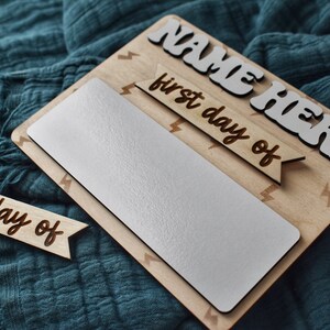 May include: Wooden sign with a white background and the text "NAME HERE" in white letters. The sign also has a wooden banner with the text "first day of" and another wooden banner with the text "last day of".