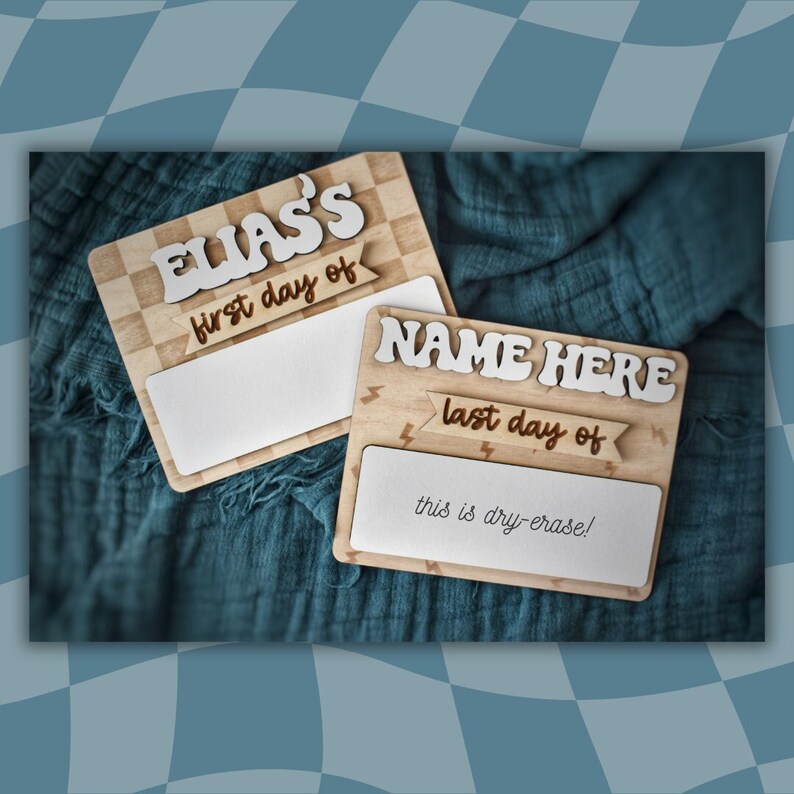 May include: Two wooden signs with a checkered pattern and lightning bolt accents. The top sign says "ELIAS'S first day of" and the bottom sign says "NAME HERE last day of" with the text "this is dry-erase!" below.