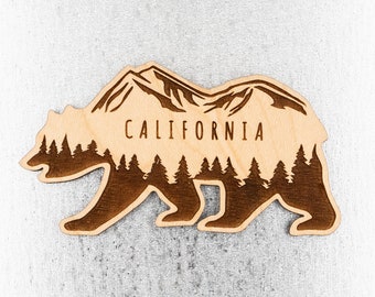 Op de afbeelding: Houten beren silhouet met een bergketen en dennenbomen in de beer. De woorden "CALIFORNIA" zijn op de borst van de beer gedrukt.