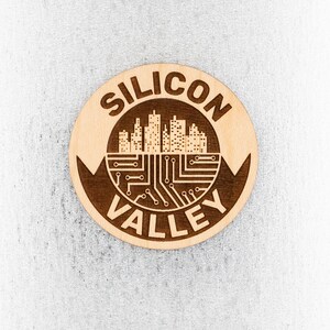 May include: A round wooden coaster with the words "Silicon Valley" and a stylized image of a city skyline with circuit board patterns.
