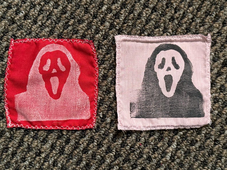 Pu&ograve; includere: Due toppe in tessuto con il design della maschera di Scream. Una &egrave; rossa con maschera bianca, l'altra rosa con maschera nera. Entrambe sono quadrate con bordi cuciti bianchi, per abbigliamento o accessori.