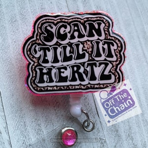 May include: A pink and black badge reel with the text "SCAN TILL IT HERTZ" in a retro font. The badge reel has a leopard print design and a clear plastic backing. The reel also has a white clip and a silver metal clasp.