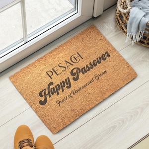 May include: A rectangular coir doormat with the text "PESACH Happy Passover Feast of Unleavened Bread" in dark brown lettering. The mat is placed in front of a door, with a pair of tan shoes visible.