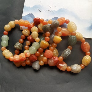 May include: A set of five bracelets made of jade beads in various colors, including green, orange, and red. The beads are carved into different shapes, including gourds, flowers, and turtles.