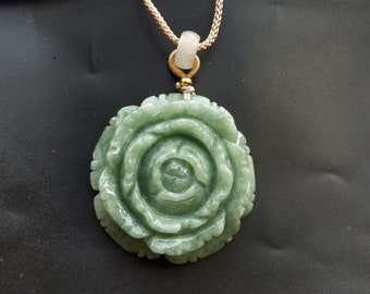 May include: A jade green rose pendant carved from jade stone. The pendant is attached to a beige cord necklace.
