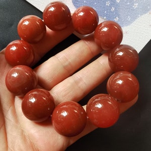 May include: A red agate gemstone bracelet with 10 round beads. The beads are polished and have a glossy finish.