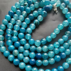 May include: A strand of turquoise blue agate beads. The beads are round and have a smooth, polished finish. The beads are strung on a clear elastic cord.
