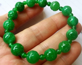 May include: A vibrant green beaded bracelet. The bracelet features round, carved beads with a floral design. The beads are strung together with smaller, round beads. The bracelet is a bright, eye-catching accessory.