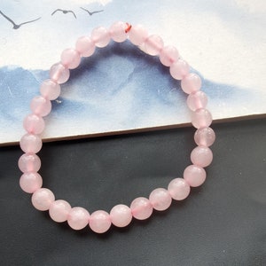 Puede incluir: Un brazalete de cuentas de cuarzo rosa con un diseño sencillo. El brazalete está hecho de cuentas lisas y redondas y está enhebrado en un cordón elástico transparente.