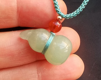 May include: A green jade gourd pendant with a light green color and a light blue cord. The pendant is tied with a light blue cord and has a red carnelian bead at the top.
