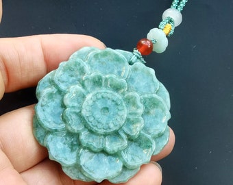 May include: A green jade pendant carved in the shape of a flower. The pendant is attached to a green cord with red and white beads.