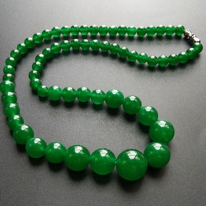 May include: A vibrant green beaded necklace with a silver clasp. The necklace features large, round beads that gradually decrease in size towards the clasp. The beads have a glossy finish and are strung together, creating a striking accessory.