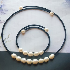 May include: Two black elastic necklaces with white pearl beads. The larger necklace has nine pearls and the smaller necklace has four pearls.