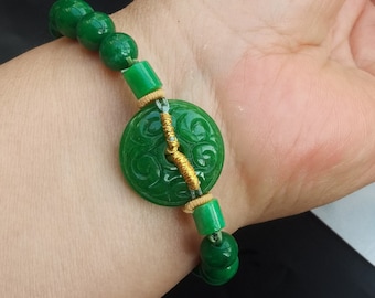 May include: A green jade bracelet with a round jade pendant featuring a carved design. The bracelet is strung with green jade beads and a gold-colored wire.