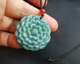 May include: A green jade pendant carved in the shape of a flower, hanging from a black cord with a red bead.