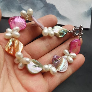 May include: A bracelet made of iridescent shell and pearl beads. The bracelet has a silver clasp and is a mix of pink, orange, and green colors.