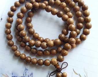 Puede incluir: Un collar de cuentas de madera marrón con un borla anudada. Las cuentas son redondas y tienen un patrón de veta de madera.