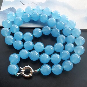 May include: A necklace of large, round, light blue beads, strung on a matching blue cord. The necklace is fastened with a silver-coloured clasp. The beads have a smooth, polished finish.