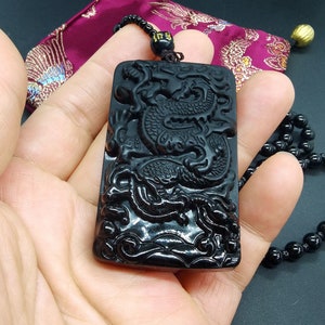 May include: Black obsidian pendant with a detailed carving of a dragon. The pendant is on a black beaded necklace.