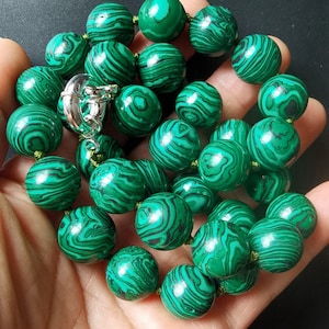 Puede incluir: Un collar de cuentas redondas de malaquita verde. Las cuentas tienen un patrón de remolino de verde oscuro y verde claro.