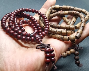 Puede incluir: Dos hileras de cuentas de madera, una marrón y otra rojo oscuro, se muestran en una mano. Las cuentas marrones están hechas de madera más clara y tienen un acabado más natural. Las cuentas rojo oscuro están hechas de madera más oscura y tienen un acabado más pulido.