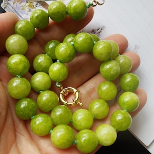May include: A necklace composed of smooth, round, light green beads strung together on a thin cord. The beads exhibit a polished, semi-translucent appearance with subtle variations in color. A gold-toned circular spring ring clasp secures the ends.