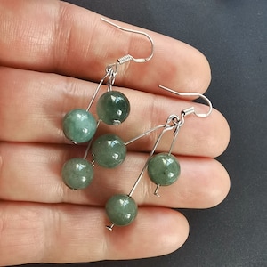 May include: A pair of dangle earrings with five green jade beads and silver hooks.