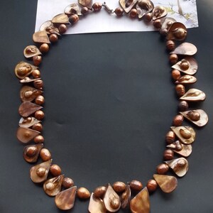 May include: A brown and gold teardrop-shaped pearl necklace with a silver clasp. The pearls are arranged in a staggered pattern.