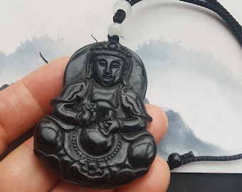 Puede incluir: Collar con colgante de jade negro que representa una figura de Buda sentado. El colgante está decorado con tallas intrincadas y un cordón negro.