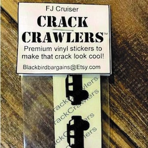 May include: Two black vinyl stickers of a side view of an FJ Cruiser with the text "CRACK CRAWLERS" and "Premium vinyl stickers to make that crack look cool!" and the website "Blackbirdbargains@Etsy.com".