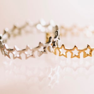 May include: Two star-shaped rings, one silver and one gold, are stacked on top of each other. The rings are made of thin metal and have a delicate design.