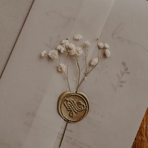 May include: A white envelope with a gold wax seal and a sprig of white baby's breath. The envelope has the word "love" written on it in cursive.