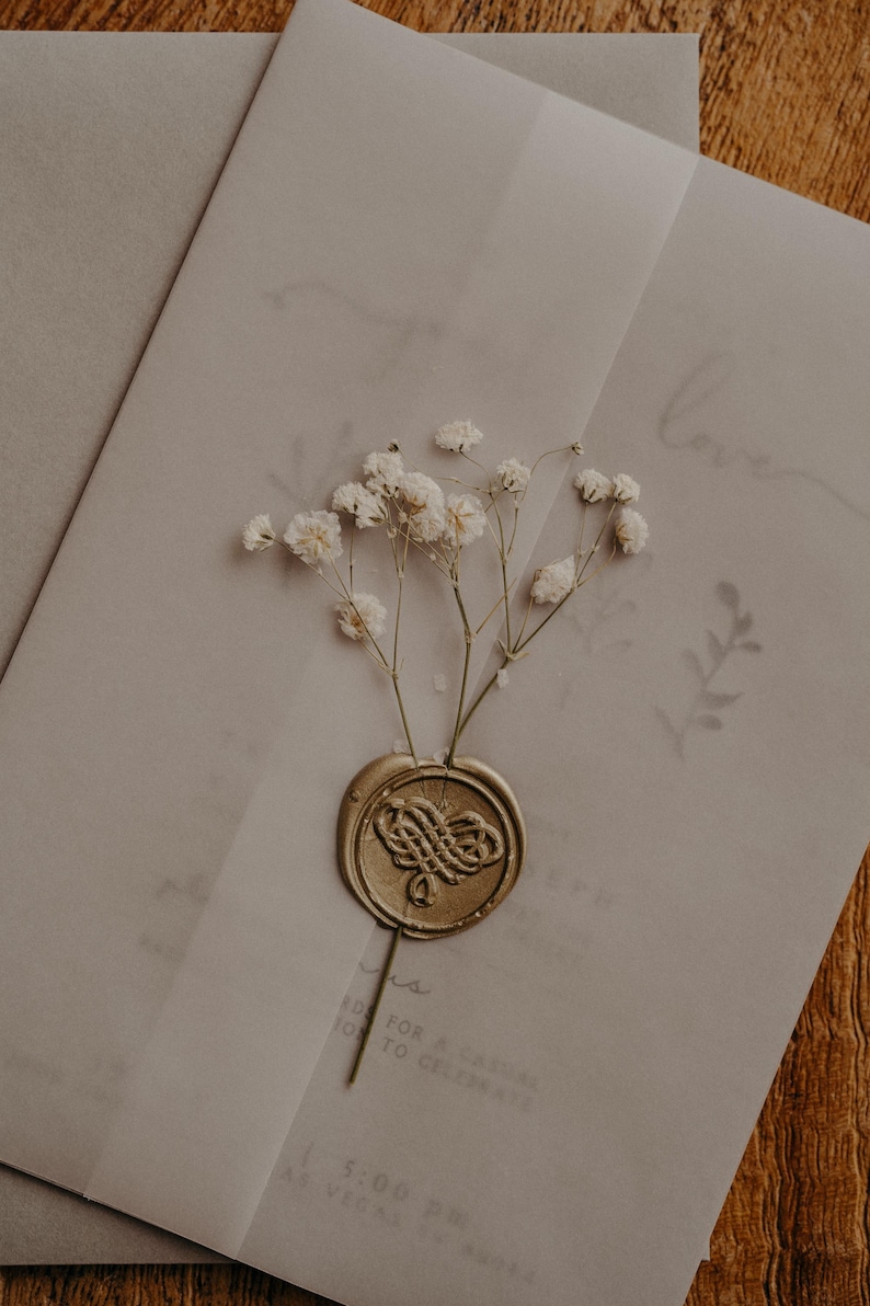 May include: A white envelope with a gold wax seal and a sprig of white baby's breath. The envelope has the word "love" written on it in cursive.