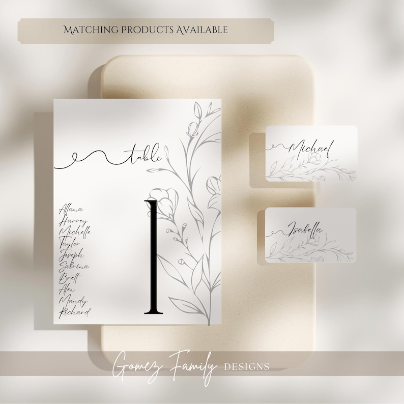 May include: A white card with a black floral design and the word "table" written in cursive. The card also has a black number "1" and a list of names. Two smaller white cards with floral designs and the names "Michael" and "Isabella" written in cursive.