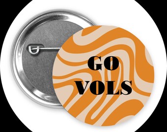 Könnte beinhalten: Ein runder Button mit silberner Rückseite und einem cremefarbenen und orangefarbenen Wirbeldesign. Der Button trägt die schwarzen Worte "GO VOLS".