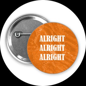 May include: A round button pin with a silver backing and a bright orange face. The face features the word "ALRIGHT" repeated three times in bold, white capital letters. The pin is set against a white background.